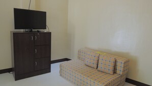 A small room with a dark wooden cabinet, a television on top, and a plaid sofa against the wall. - Pedz Cing Mango Lodge (Oslob)