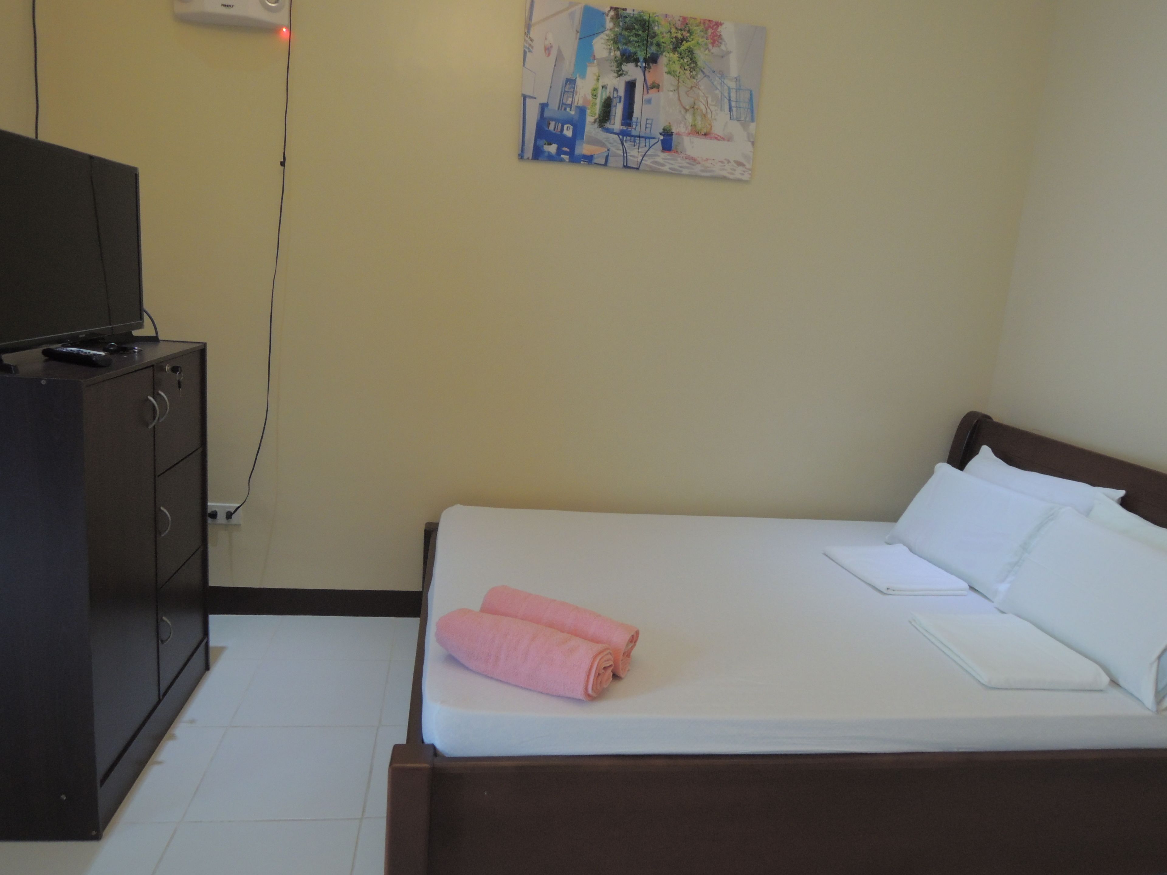 A bedroom with a bed, a dresser, a painting on the wall, and a TV on a cabinet.