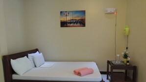 A single bed with white bedding, a wooden headboard, and a pink towel. A small table with a plant and a figurine is beside the bed. - Pedz Cing Mango Lodge (Oslob)