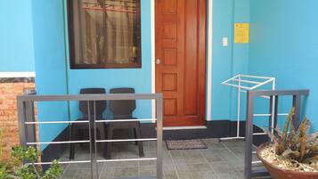 A blue building with a wooden door, two wicker chairs, a metal gate, and a potted plant.