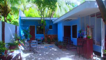 Una casa azul con un patio, rodeada de plantas en macetas y un pequeño jardín.