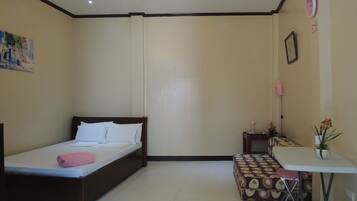A room with a bed, a small table, a chair, a lamp, and a wall clock.