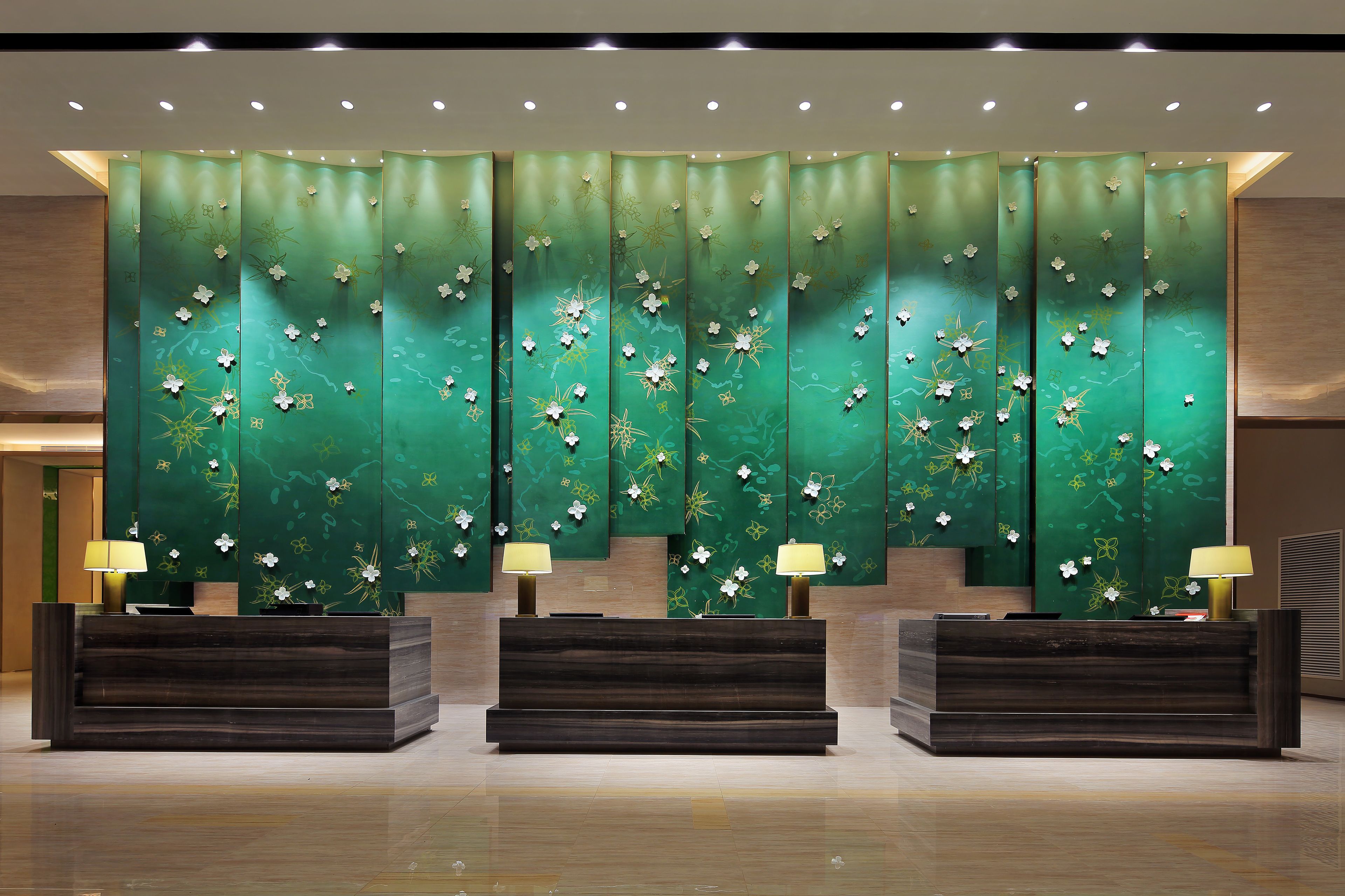 Un área de recepción con un fondo floral verde, dos mostradores de recepción y dos lámparas.