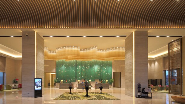 Un hall amplio con diseño moderno, que incluye una recepción, zona de estar y una pared decorativa con motivos florales.
