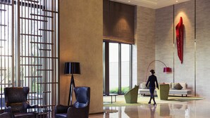 Un lobby espacioso con diseño moderno, que incluye una gran mesa de madera, zona de estar con sillas y un amplio ventanal que proporciona luz natural.