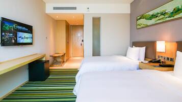 Une chambre d’hôtel avec deux lits, un téléviseur fixé au mur, un bureau et une poubelle.