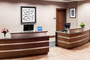 A reception area with two wooden reception desks, a digital screen, framed artwork, and a door. - Residence Inn by Marriott Dallas Plano/Richardson (Plano)