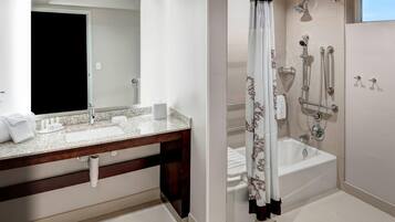 A bathroom with a large mirror, a sink, a bathtub, and a shower area.