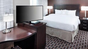 A hotel room with a bed, a desk with a flat-screen TV, a lamp, and a bedside table. - Residence Inn by Marriott Dallas Plano/Richardson (Plano)