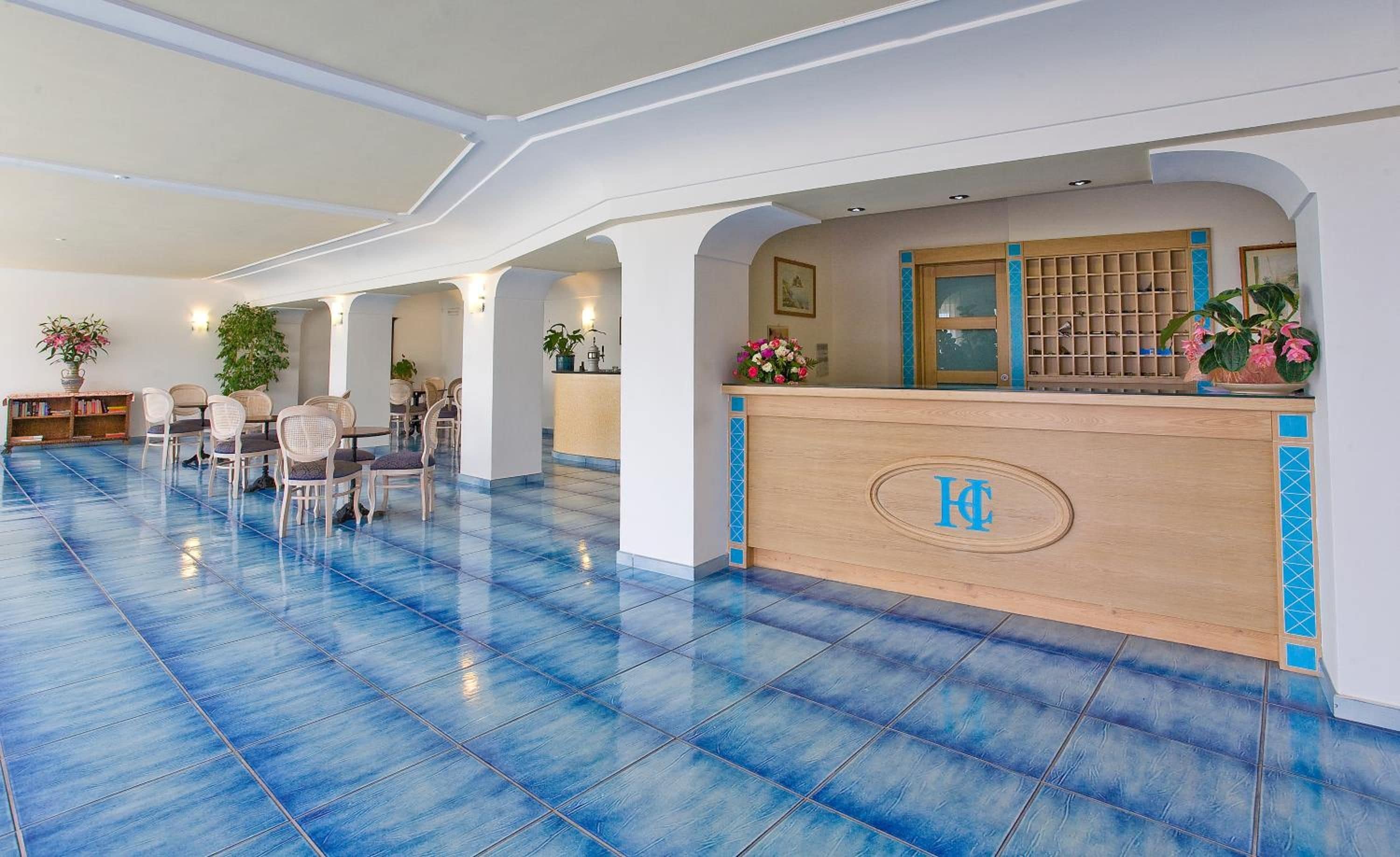 Un vestíbulo de hotel con mostrador de recepción, zona de estar y suelo de baldosas azules.