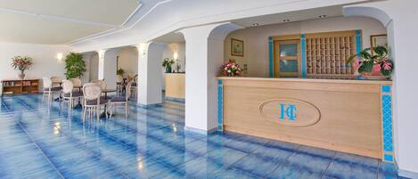 Un vestíbulo de hotel con mostrador de recepción, zona de estar y suelo de baldosas azules.