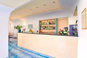 A bar area with a counter, shelves of bottles, a potted plant, and a dining area with chairs.