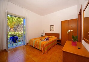 A bedroom with a bed, a desk, a chair, a wardrobe, and a sliding glass door leading to an outdoor area with a table and chairs.