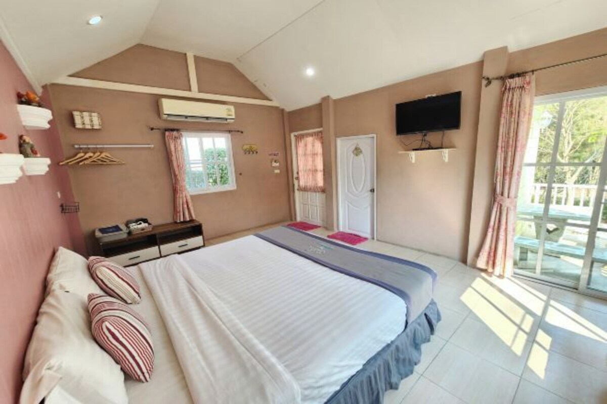 A bedroom with a bed, a dresser, a TV, and a window with curtains.
