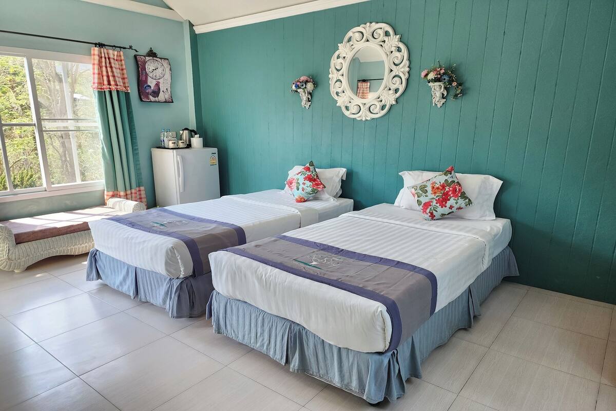 A bedroom with two beds, a window with curtains, a mirror, and a small table.