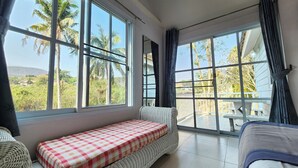 A room with a large window, a checkered bed, wicker furniture, and a view of palm trees. - See Sky Resort (Pak Chong)