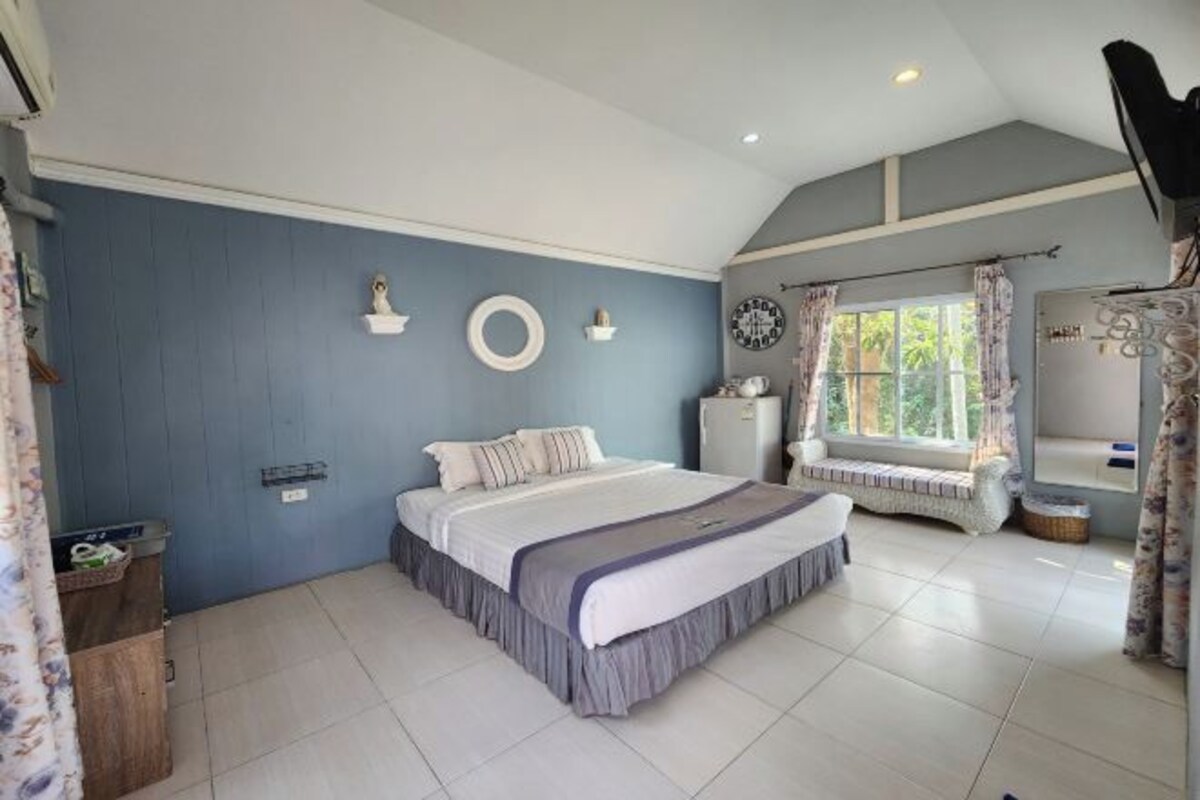 A bedroom with a bed, a bench, a wardrobe, and a window with curtains.