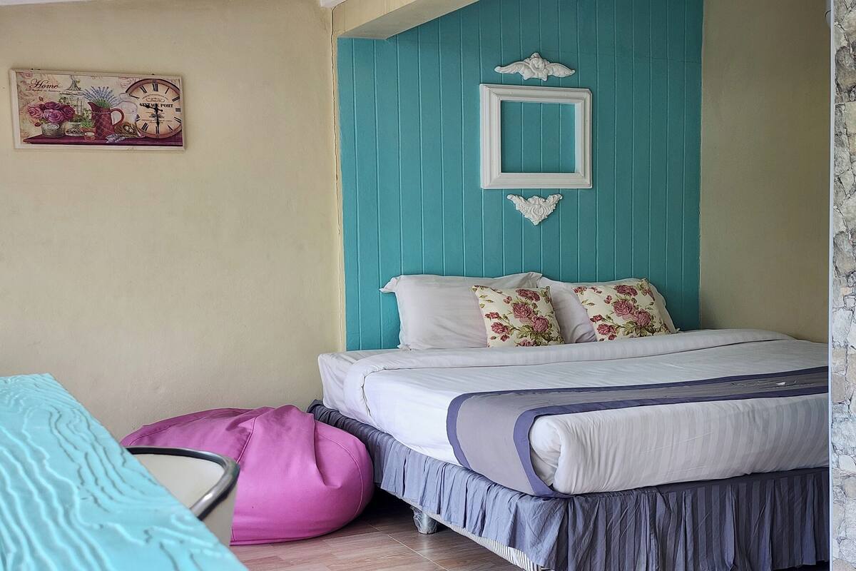 A bedroom with a bed, a pink bean bag, and a teal wall.