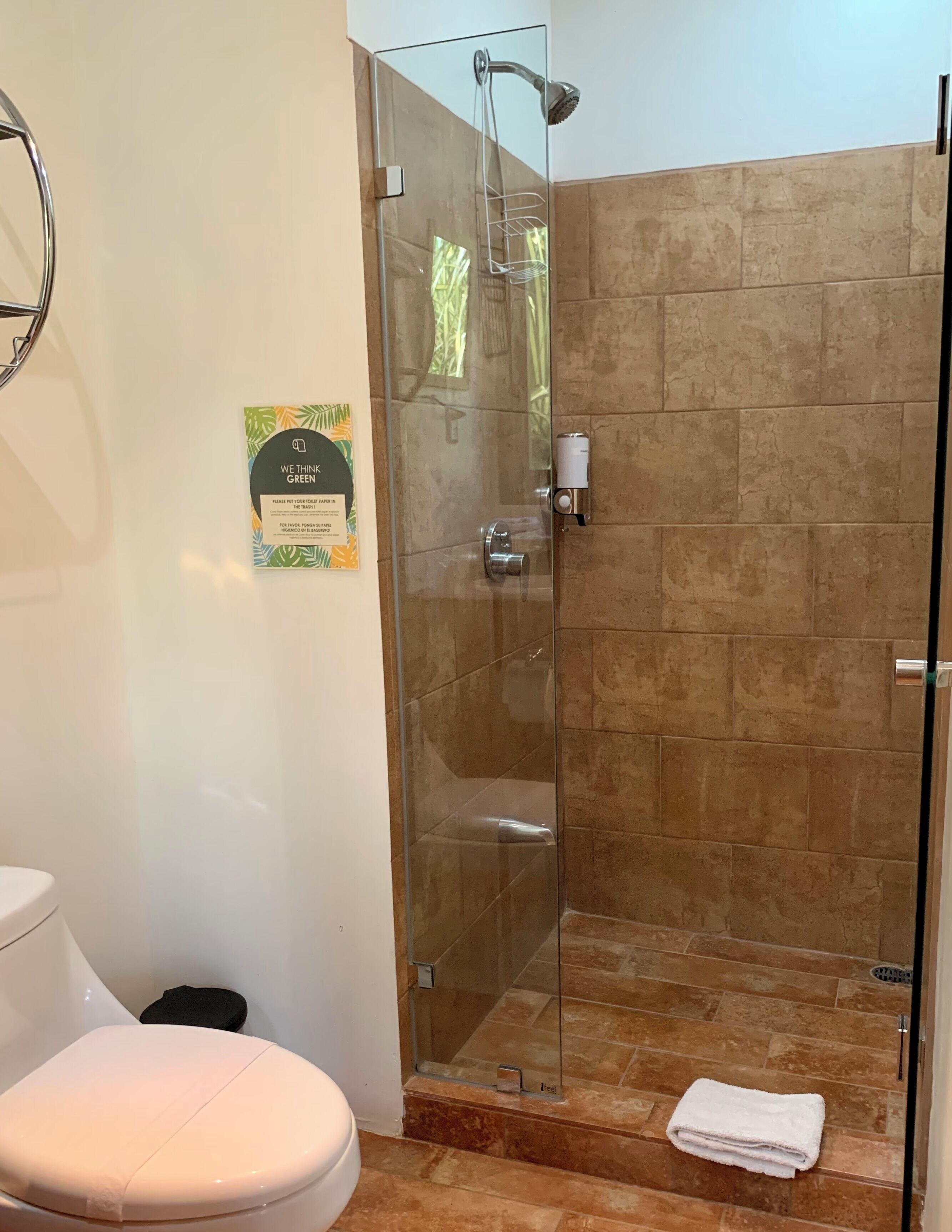 A bathroom with a glass-enclosed shower, a toilet, and a towel on the floor.