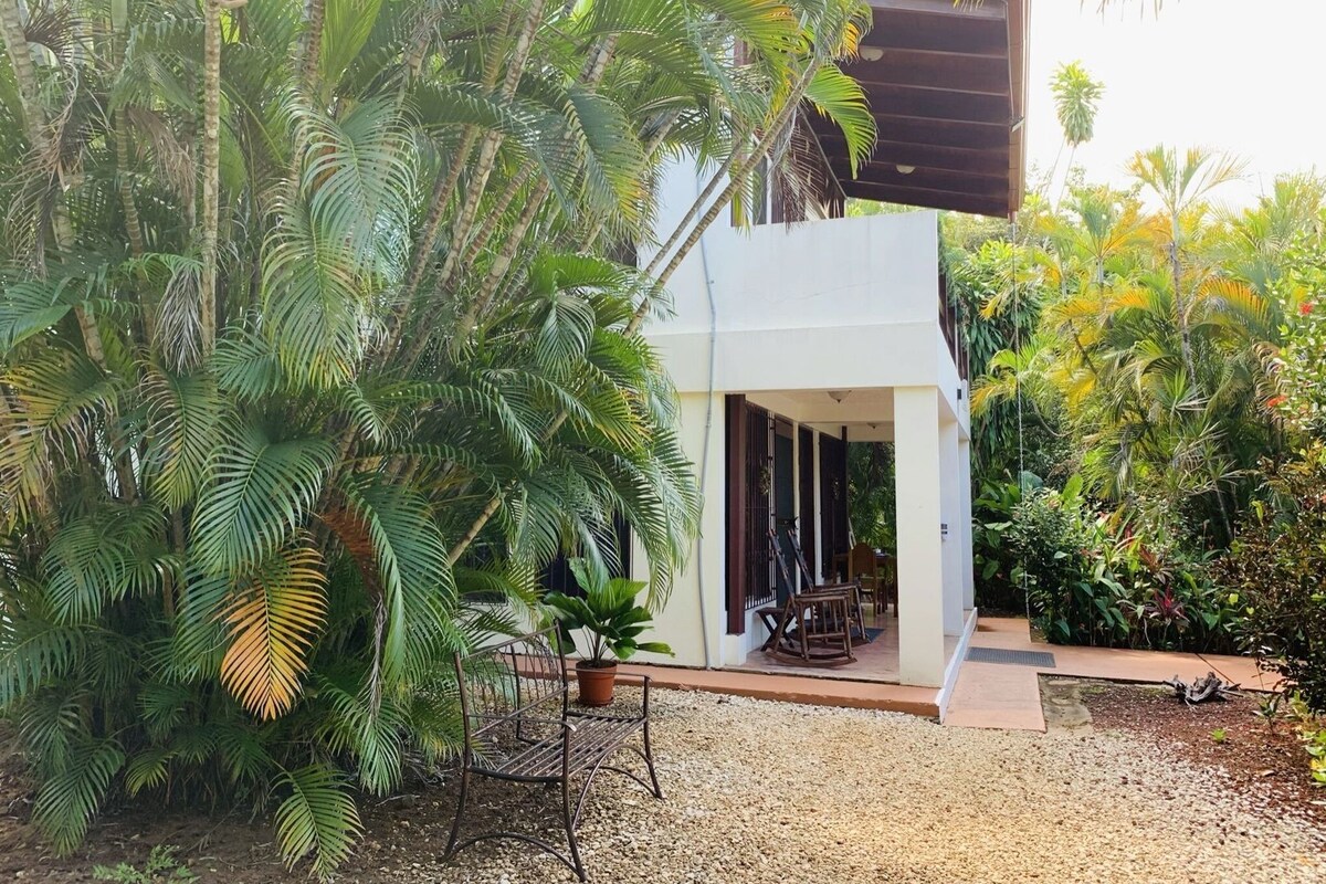 A two-story building with a covered outdoor seating area, surrounded by dense tropical vegetation.
