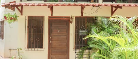 Um edifício com porta de madeira, varanda com guarda-corpo e plantas em vasos.