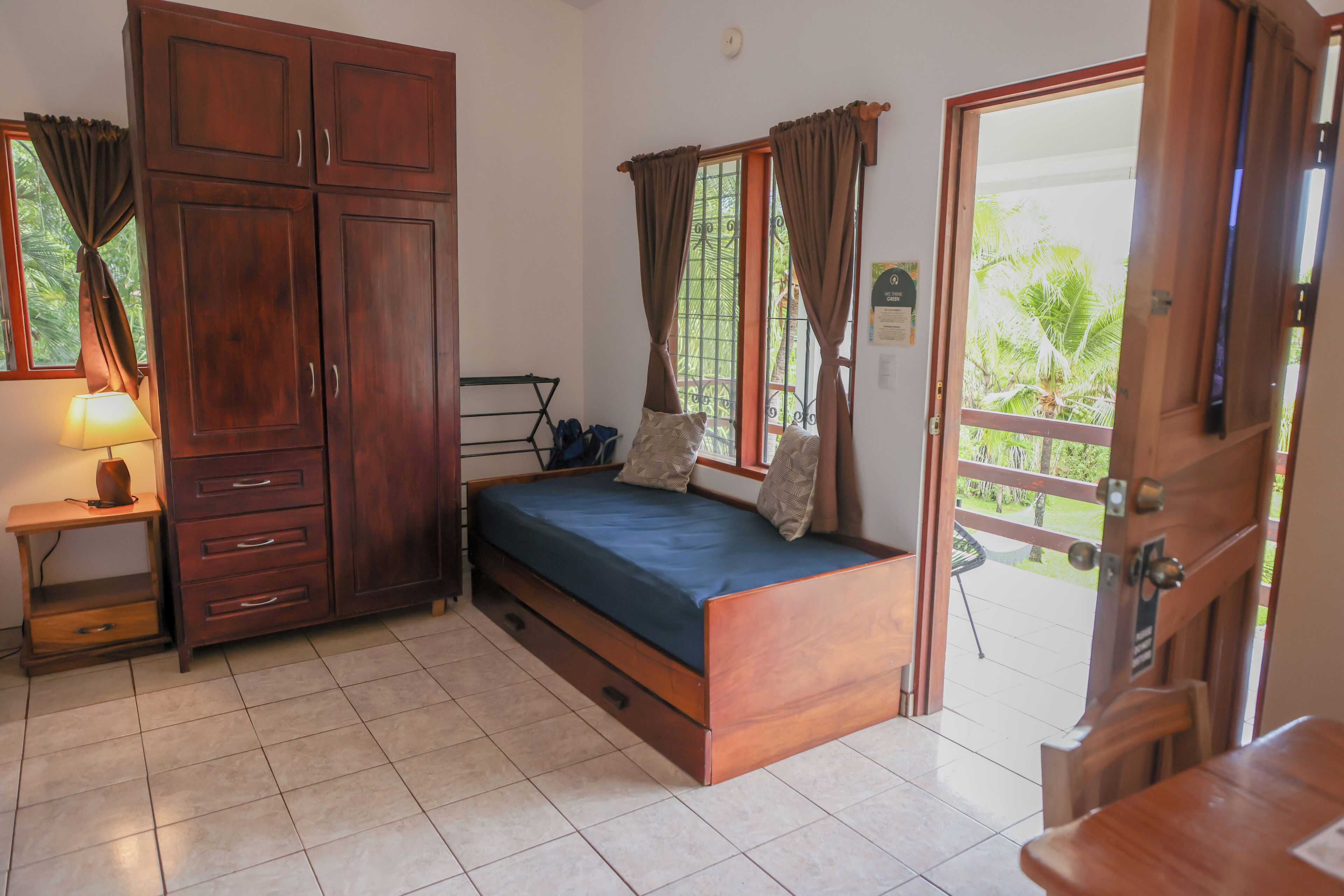 A bedroom with a bed, wooden wardrobe, and a small table with a lamp.