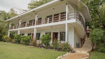 A two-story building with a balcony on the upper floor, surrounded by lush greenery and a well-maintained lawn.