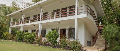 A two-story building with a balcony on the upper floor, surrounded by lush greenery and a well-maintained lawn.