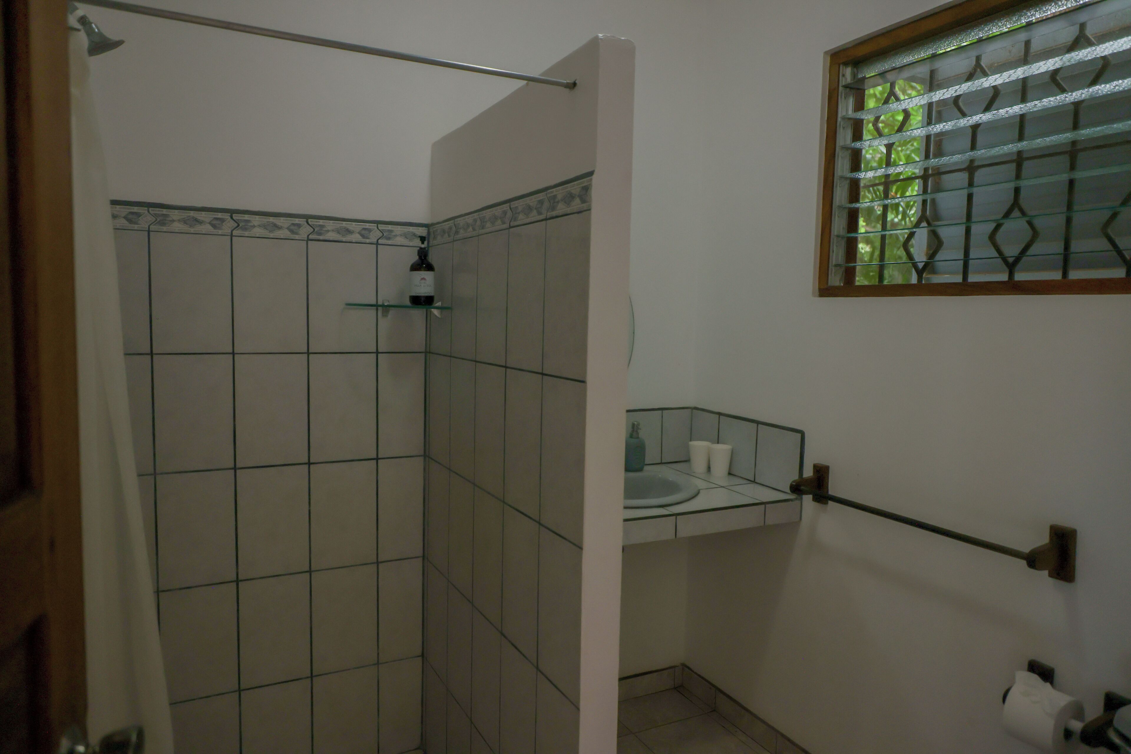 A bathroom with a shower, a glass sink, and a window with metal bars.