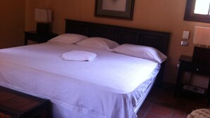 A neatly made bed with white linens and a folded towel, a framed floral artwork on the wall, and a nightstand with a lamp. - Cabinas Cigalou Tamarindo (Tamarindo)