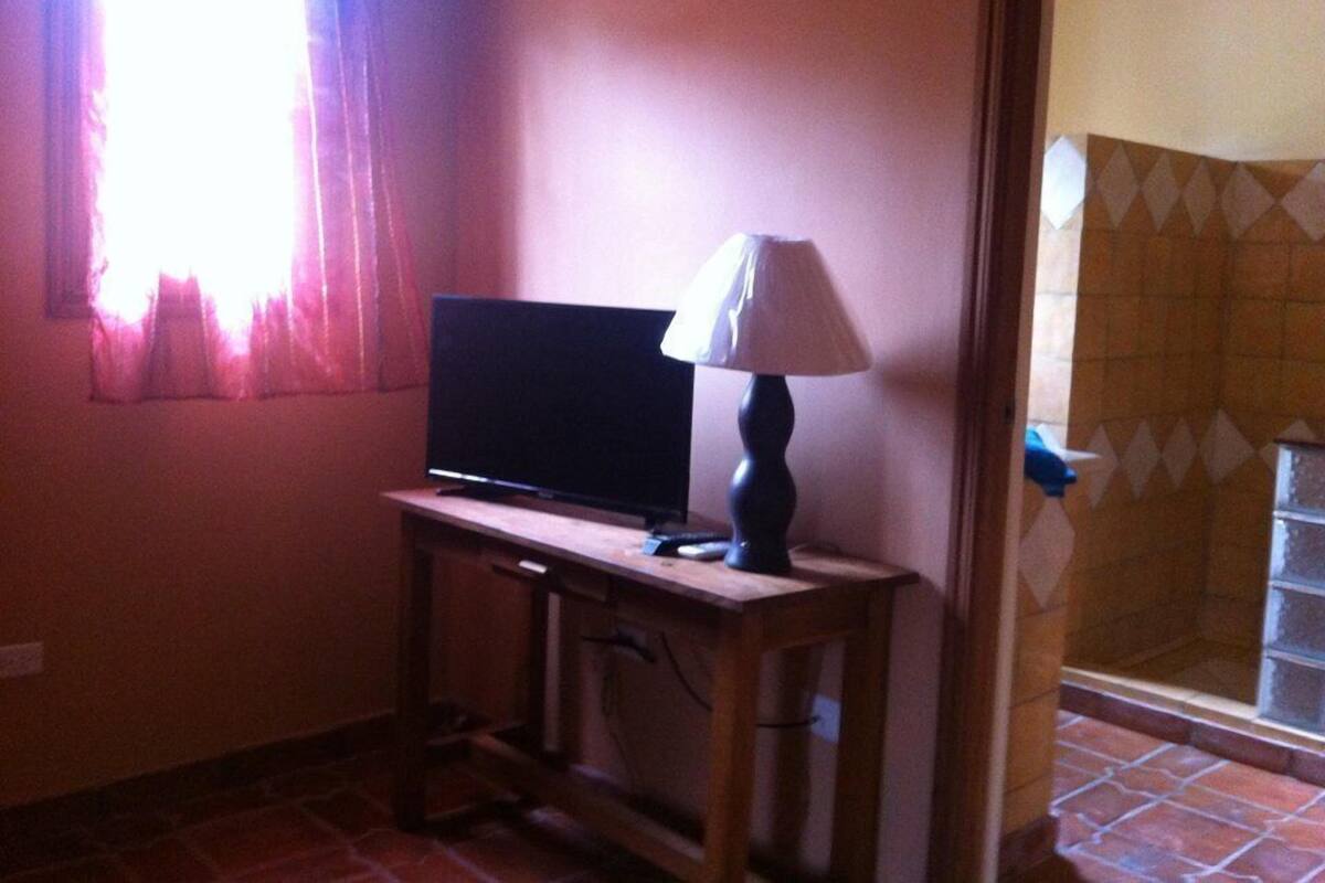 A room with a television on a wooden table, a lamp, and a window with curtains.