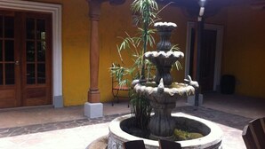 A courtyard with a stone fountain, a wooden door, and a yellow wall. - Cabinas Cigalou Tamarindo (Tamarindo)