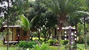 A rustic lodge with a thatched roof, surrounded by lush greenery and a small pond with ducks. - Banana House Pai (Pai)