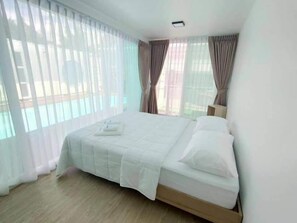 A hotel room with a large bed, white bedding, and sheer curtains.