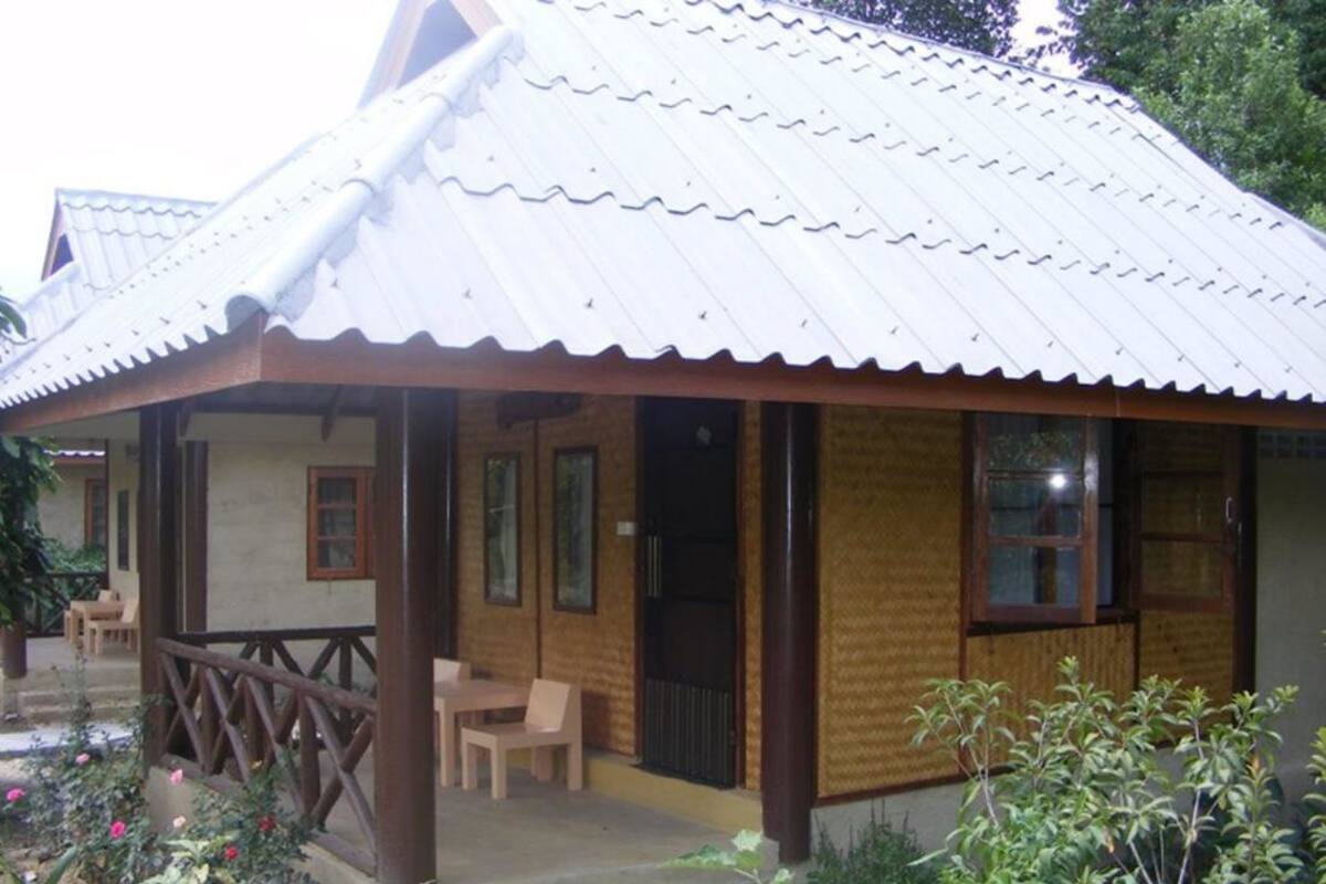 A wooden structure with a metal roof, a covered porch, and a garden area with plants and flowers.