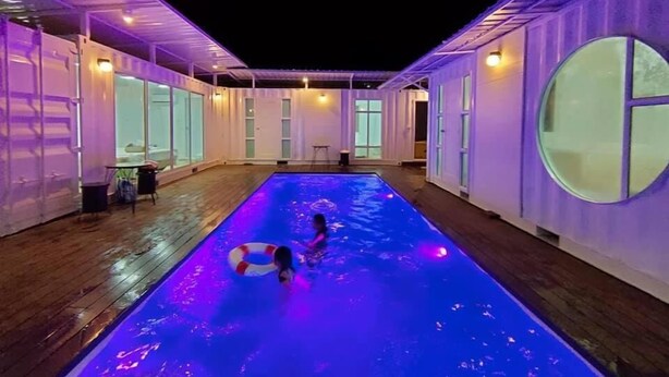 A swimming pool with a person in it, surrounded by a covered area with glass doors and windows. - Banana House Pai (Pai)