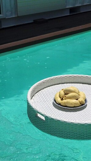 A pool with a circular floating lounge chair containing a bowl of bananas.
