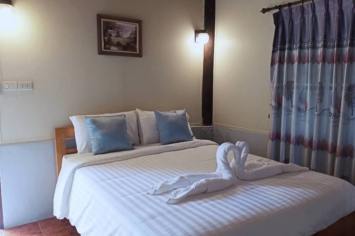A neatly made bed with a striped bedspread and two pillows, a framed picture on the wall, and a curtain with a tree design.