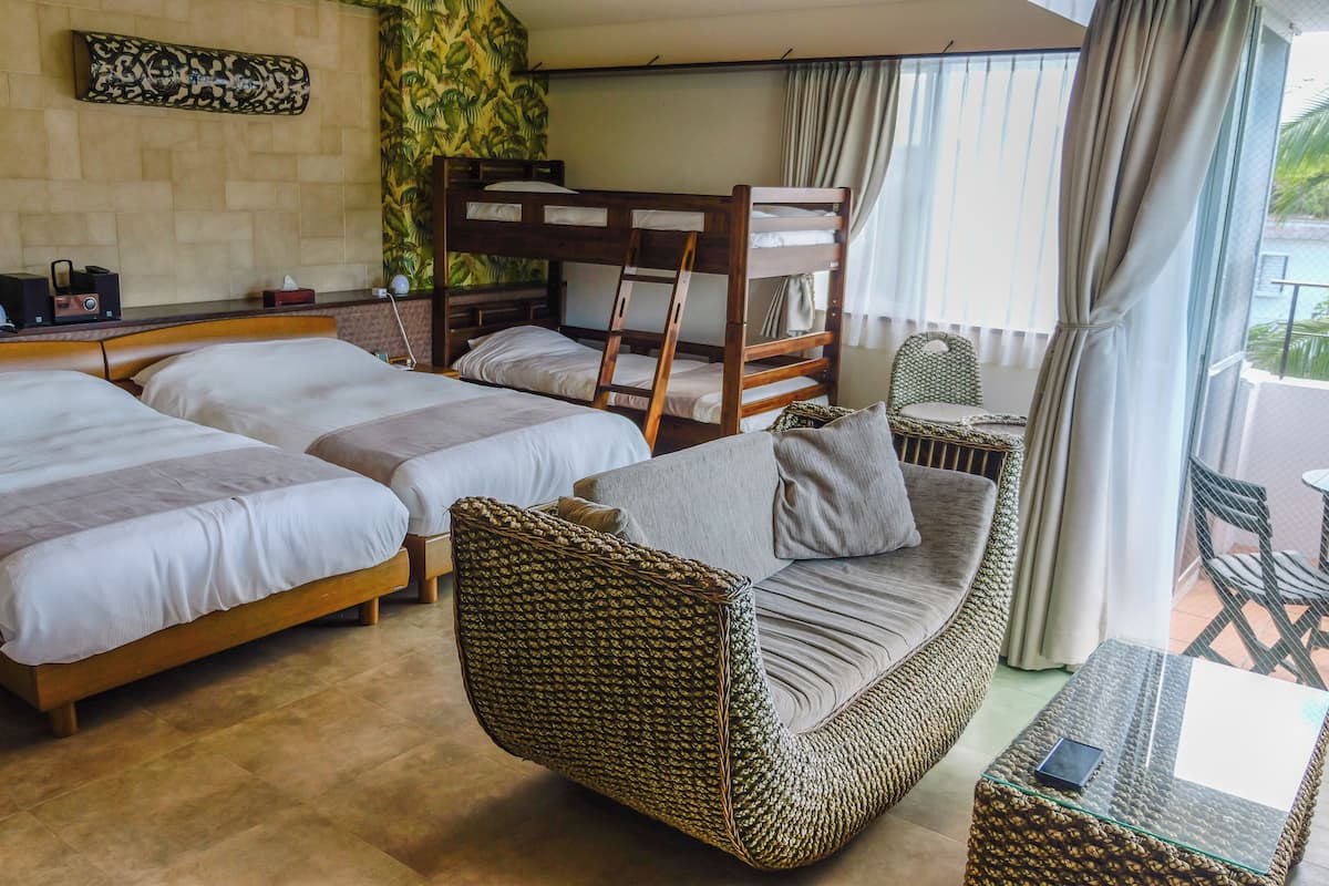 Une chambre d’hôtel avec deux lits, un canapé, un balcon avec une table et un mur décoré de motifs.