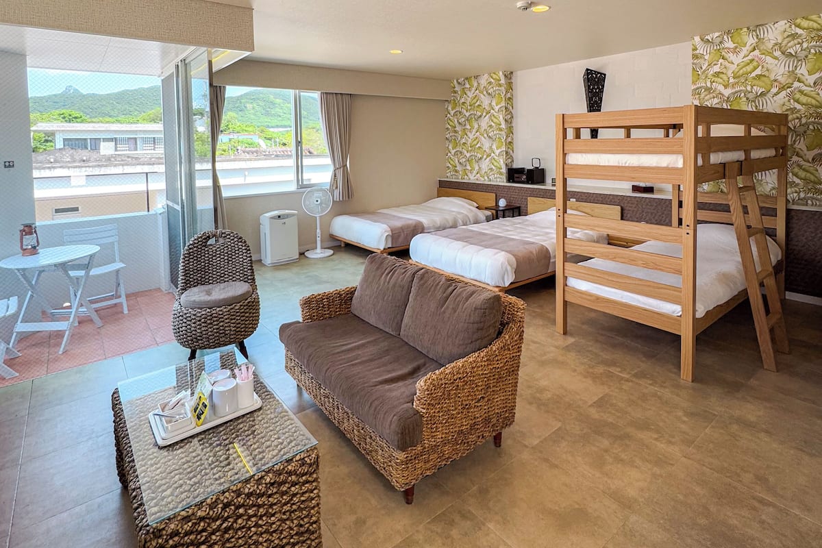 Une chambre d’hôtel avec un balcon, un canapé, un lit, un bureau et un lit superposé.