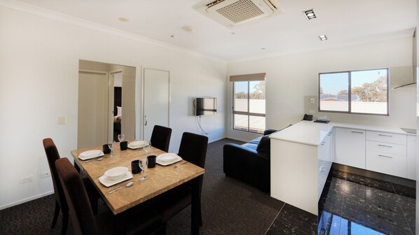 A modern hotel room with a dining area, a kitchenette, and a TV mounted on the wall.