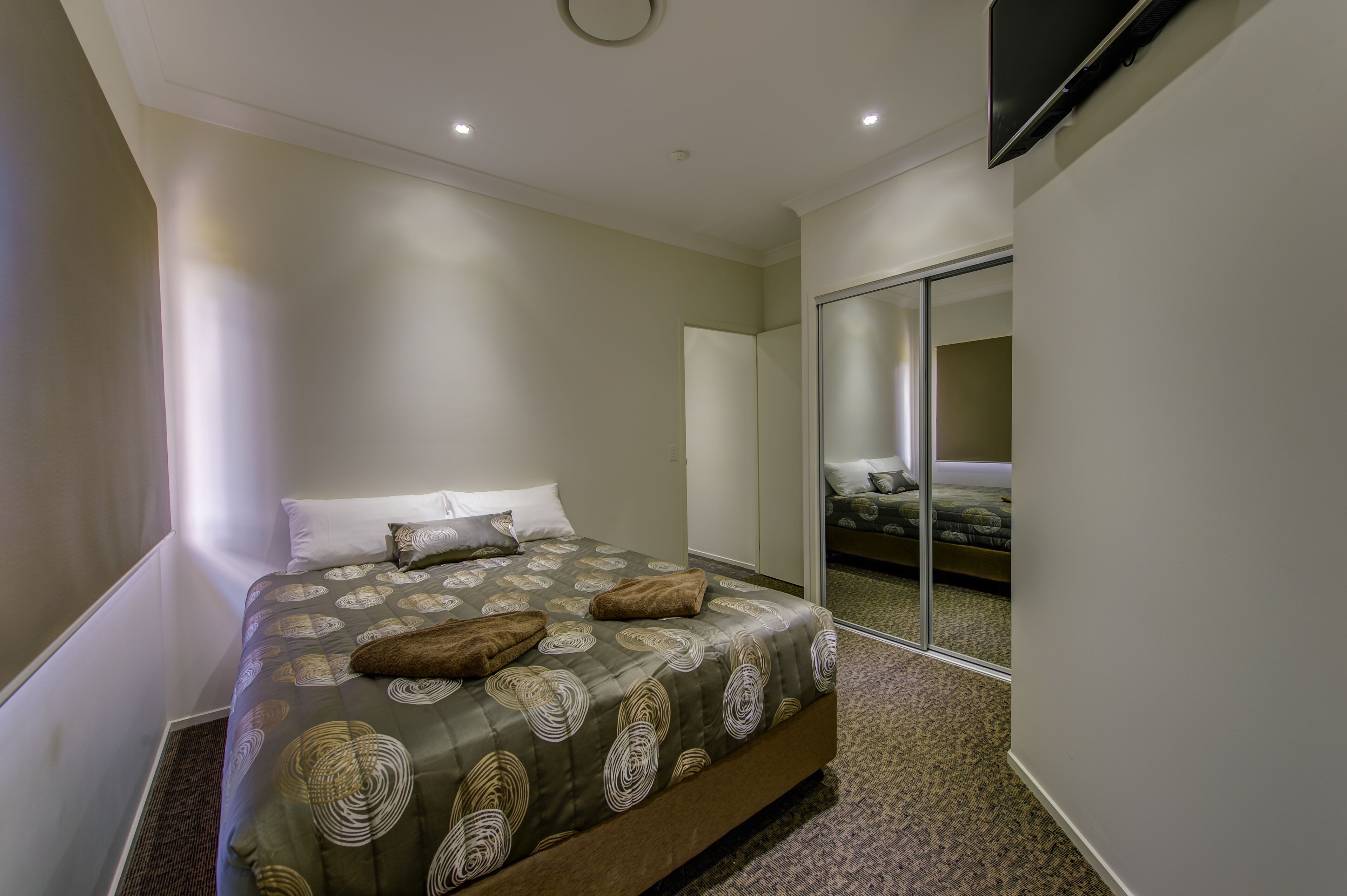 Ein modernes Hotelzimmer mit einem großen Bett, einem Flachbildfernseher und einer Glastür, die auf einen Balkon führt.