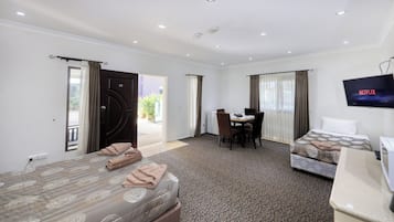 A hotel room with two beds, a desk, a chair, a TV, and a balcony door.