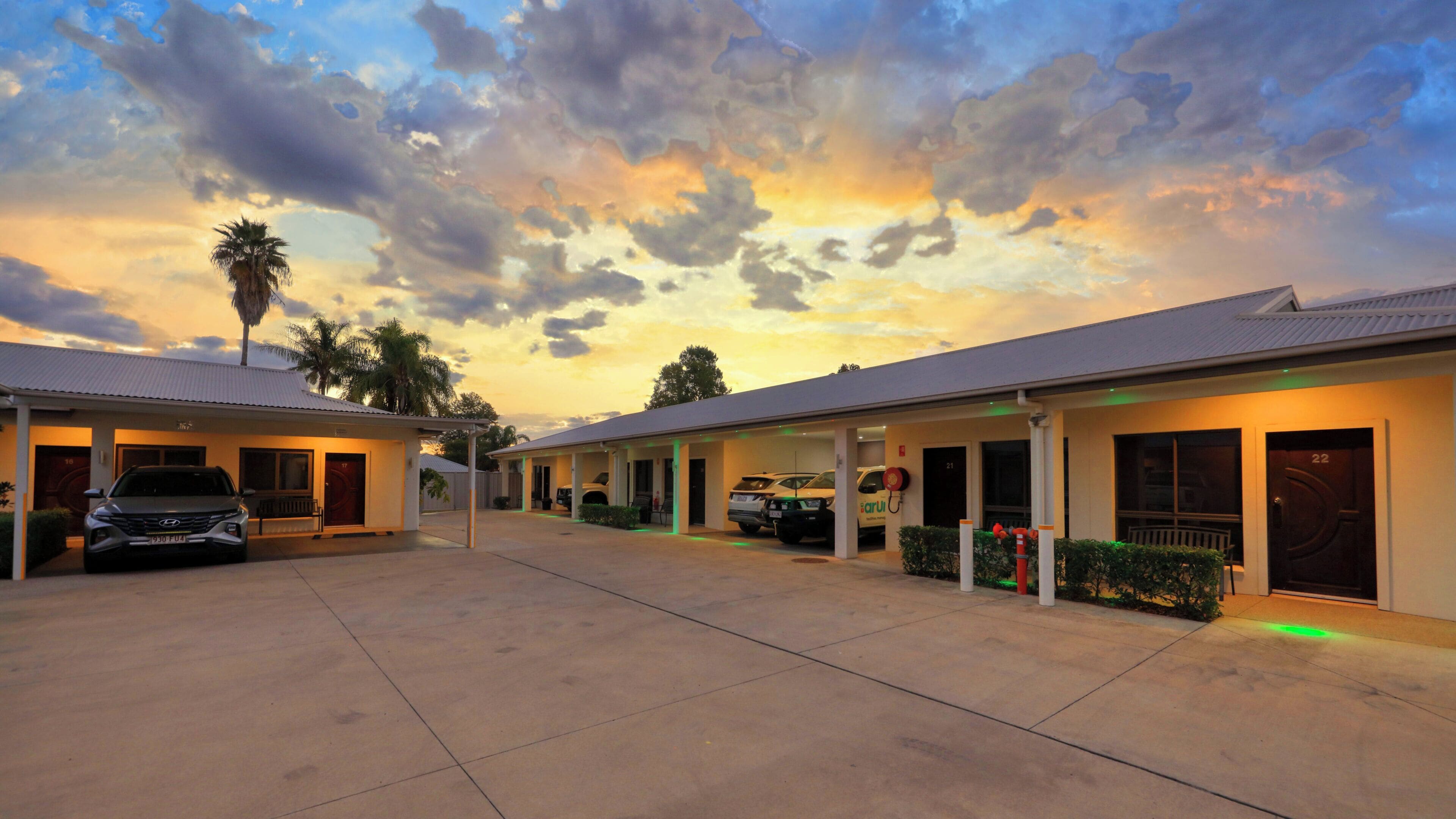 A hotel with a covered parking area, multiple rooms, and a sunset sky.