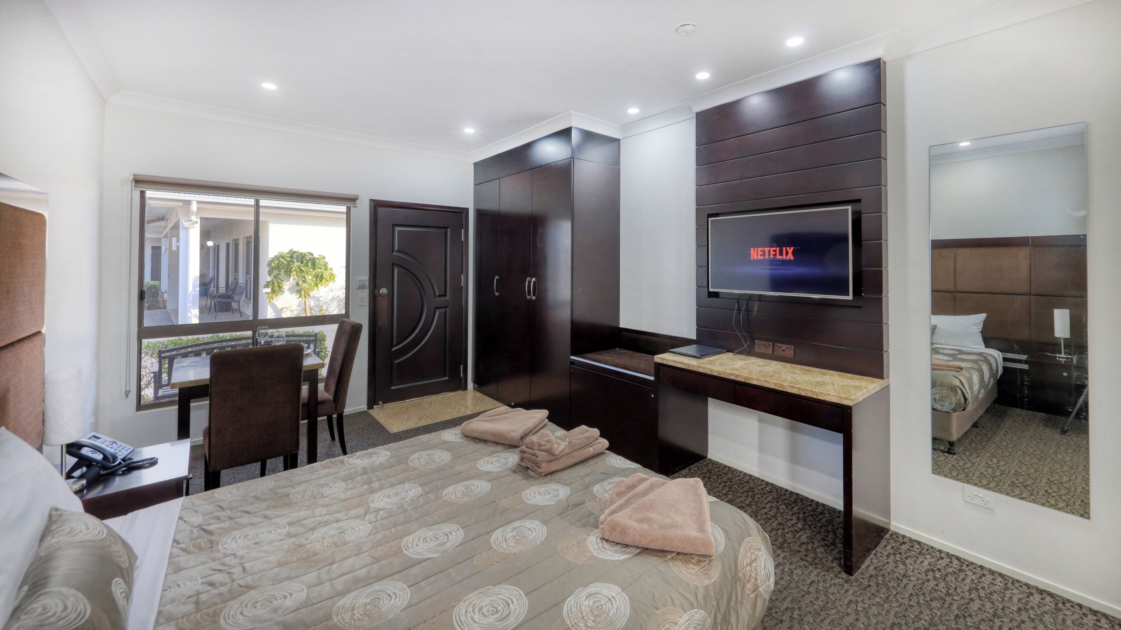 Une chambre d’hôtel avec un lit, un bureau avec une télévision, une chaise, une fenêtre et une porte.