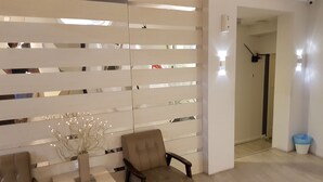 Una habitación moderna con un panel reflectante, un sillón acolchado, una mesita y un florero con ramas.