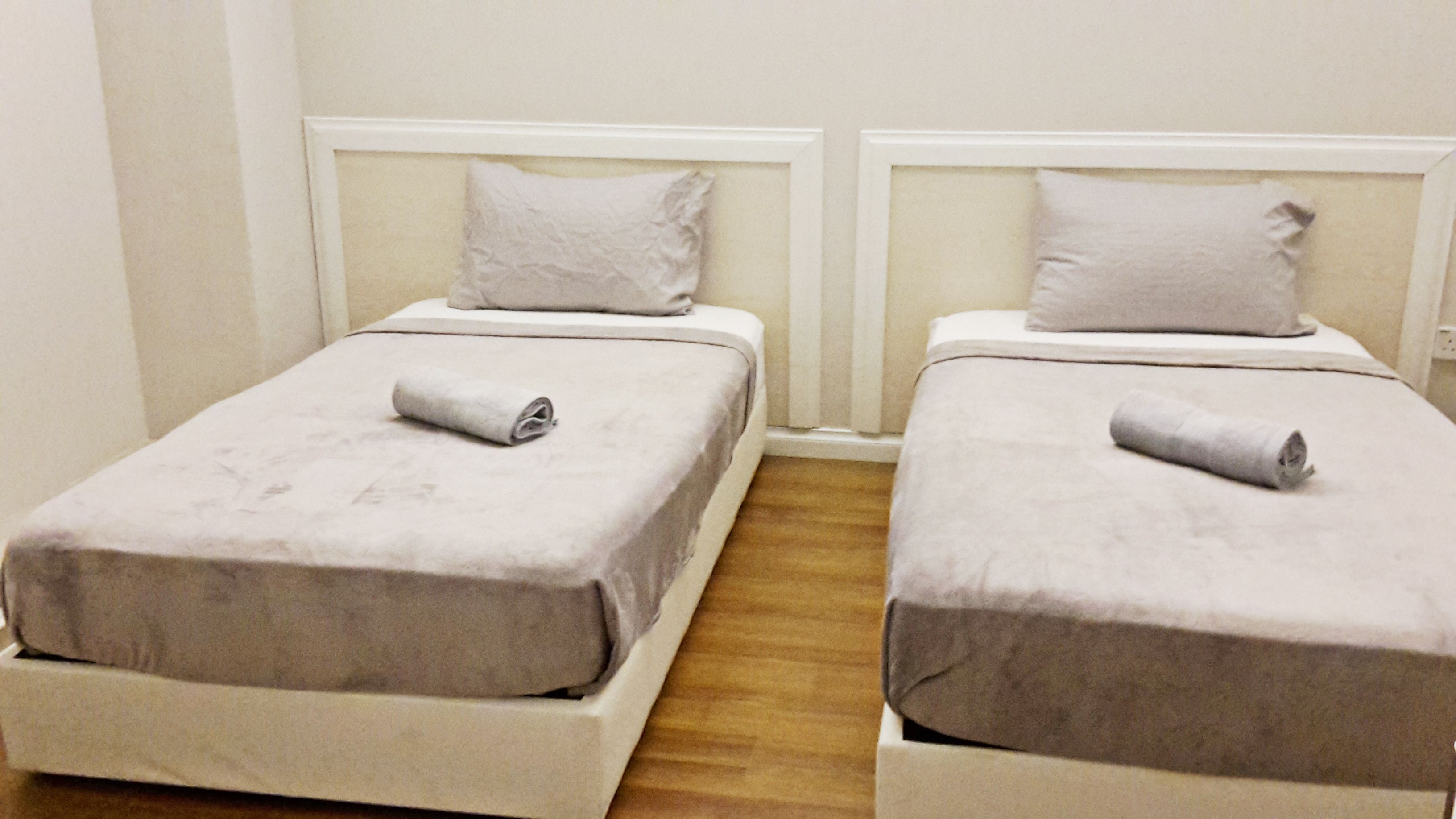 Two single beds with white bedding and pillows, wooden flooring, and white headboards.