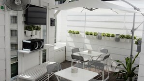 A patio area with white furniture, a fan, and potted plants. - Travelogue KL - Hostel (Kuala Lumpur)
