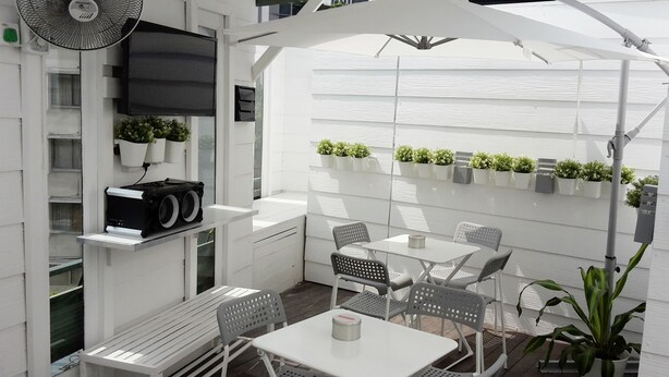 Un patio con mobiliario blanco, un ventilador y plantas en macetas.