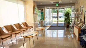 A hotel lobby with a reception desk, a green exit sign, and a seating area with chairs and tables. - AZ Inn Handa Inter (Handa)